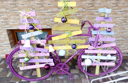 Old bicycle decorated with improvised Christmas trees standing at the wall of the buildingの写真素材
