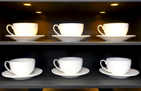 White cups and saucers stand in rows on shelves in a restaurantの写真素材