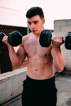 fitness guy doing exercises with dumbbells outdoorsの写真素材