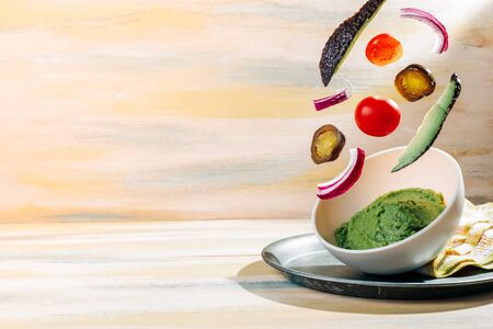 Homemade guacamole bowl with ingredients floating around it. Vintage wooden table. Healthy foodの写真素材