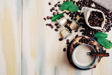 Coffee beans on vintage light wooden table, with coffee capsule and a cup of coffee. Top view. Copyspace.の写真素材