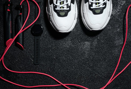 sneakers, jump rope and watch on dark background, with copyspace
