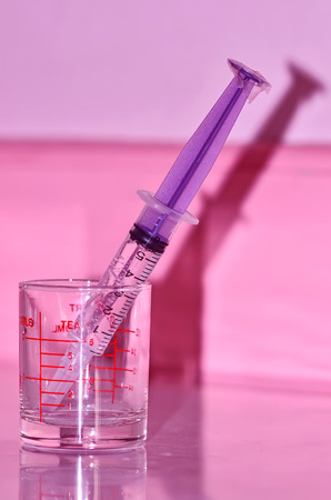 Syringe and a glass measuring cup on pink backgroundの写真素材
