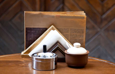 Sugar-bowl, napkin, newspaper and ash tray on the wooden tableの写真素材
