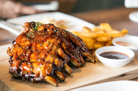 Close up Gourmet Grilled Pork Rib and Fried Potato Wedges on wood Plate with Sauceの写真素材
