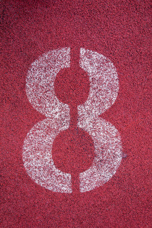 Number eight on running track. White track number on red rubber racetrack, texture of running...