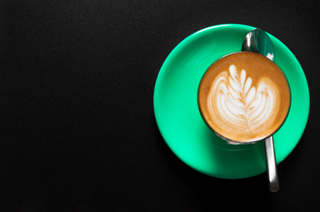 Hot latte in green cup with floral pattern in foam top view on a dark backgroundの写真素材