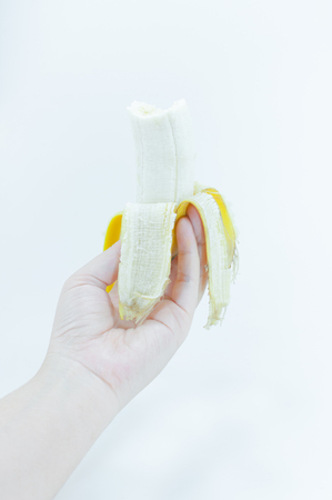 The peeled banana in a female hand holding on white background,banana fruitsの写真素材