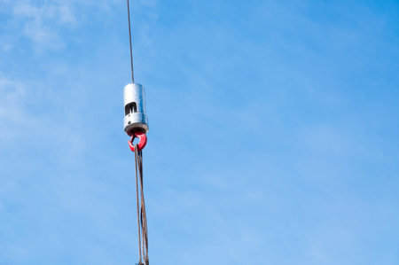 The hook of elevating crane lifts a concrete plate against the blue sky, close up