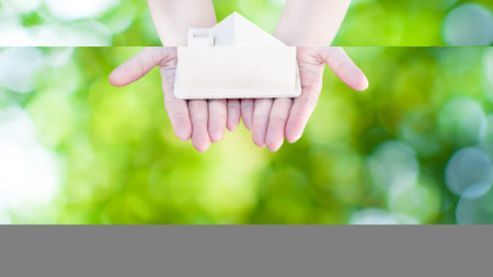 Woman hand holding small home model wooden with nature green bokeh abstract background. Family life and Business real estate concept,Eco houseの写真素材