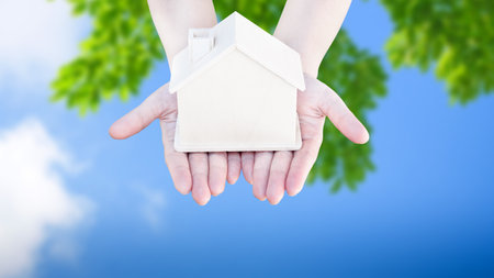 Woman hand holding small home model wooden with nature green abstract background. Family life and Business real estate concept,Eco houseの写真素材
