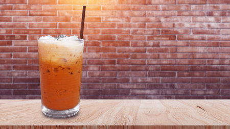 Iced thai milk tea in glass, Milk ice tea, Cheddar is a traditional Thai drink on wooden table with brick wall background, Summer drinks with icedの写真素材