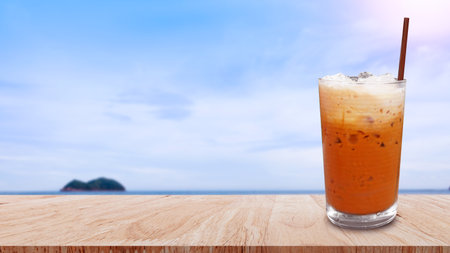 Iced thai milk tea in glass, Milk ice tea, Cheddar is a traditional Thai drink on wooden table with beach landscape nature background, Summer drinks with icedの写真素材