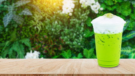 Iced matcha green tea latte with milk foam in takeaway cup on wooden table, Summer drinks with iced