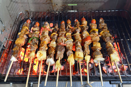 kebabs skewered with peppers and tomato sizzling over the coals of a barbecueの写真素材