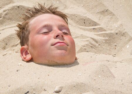 Boy buried in sand on a beach in the summerの写真素材