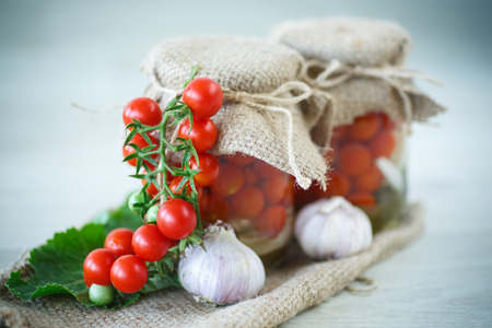 tomatoes marinated in jars with spices on a wooden tableの写真素材