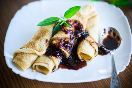thin fried pancakes stuffed with jam in a plate on a wooden tableの写真素材
