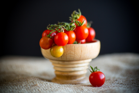 small ripe red cherry tomatoes in a wooden bowl on a tableの写真素材