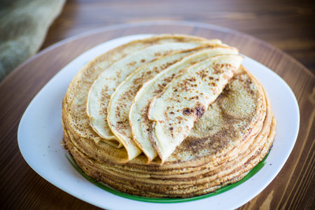 big high stack of thin pancakes in a plate on a wooden table