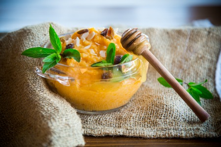 boiled sweet pumpkin porridge with raisins and nuts in a glass bowl on wooden backgroundの写真素材