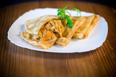 thin fried pancakes stuffed with stewed cabbage in a plate on a wooden tableの写真素材