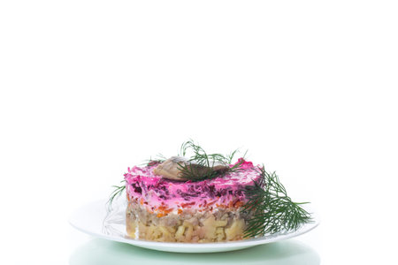 layered salad of boiled vegetables with beets and herring on a plate with greens