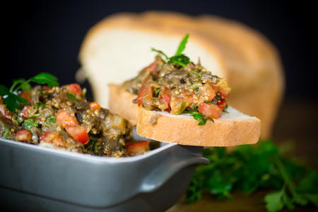 eggplant caviar with tomatoes and a slice of bread on a wooden tableの写真素材