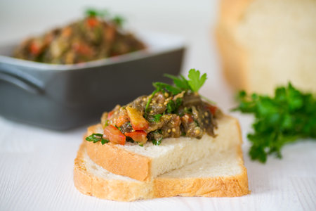 eggplant caviar with tomatoes and a slice of bread on a wooden tableの写真素材
