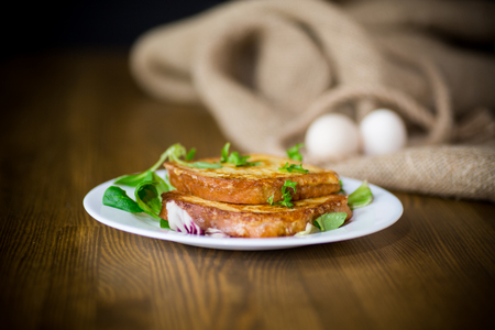 fried croutons in eggs with greens in a plate on a wooden tableの写真素材