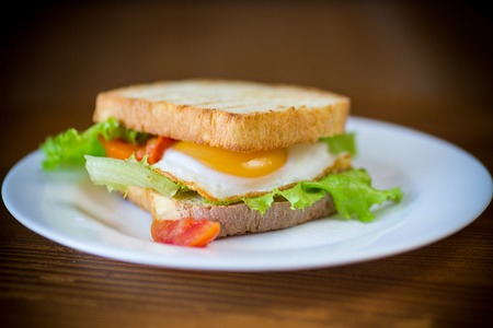 fresh sandwich with lettuce leaves and fried egg with hot toastsの写真素材