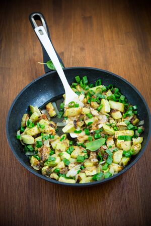 zucchini fried with onions and herbs in a pan on a wooden tableの写真素材