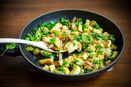 zucchini fried with onions and herbs in a pan on a wooden tableの写真素材