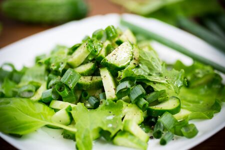 fresh salad of cucumbers and greens in a plate on a woodenの写真素材