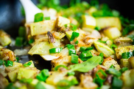 zucchini fried with onions and herbs in a pan on a wooden tableの写真素材