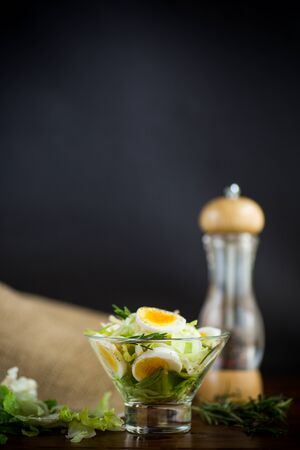 Fresh spring salad with cabbage, lettuce and boiled eggs with rosemary and spices on a wooden tableの写真素材