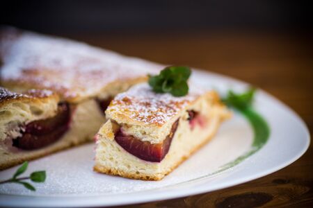 sweet baked homemade plum cake with icing sugar on a wooden tableの写真素材