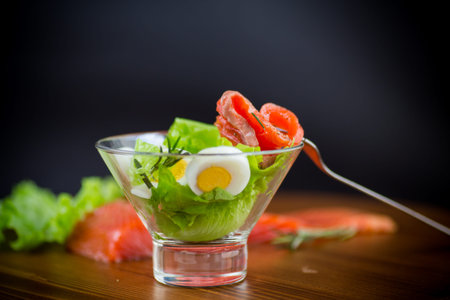 lettuce salad with salted salmon, boiled eggs on a wooden table.