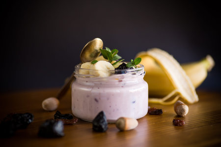 Sweet tasty yogurt with banana, prunes, raisins in a glass jar on a wooden table