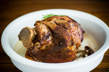 baked pork shank with spices in ceramic form, on a wooden tableの写真素材