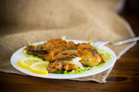 fried hake fish in batter with lettuce and lemon in a plate on a wooden table