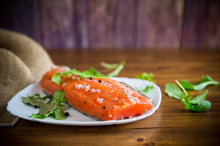 piece of salty red fish with different seasonings and herbs in a plate on a wooden table
