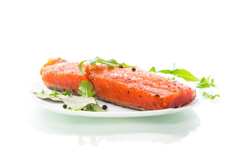 piece of salty red fish with different seasonings and herbs in a plate isolated on white background