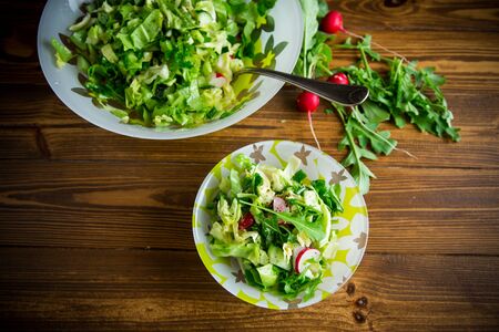 Spring salad from early vegetables, lettuce leaves, radishes and herbs in a plate on the wooden tableの写真素材
