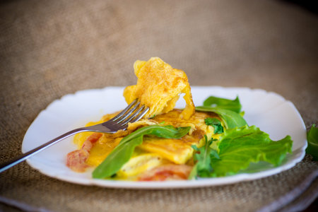 fried home omelet with vegetables and arugula in a plate on a wooden table