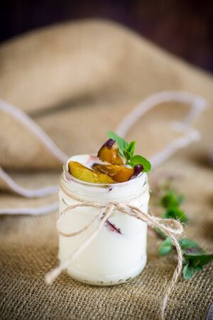 Homemade sweet yogurt with slices of ripe plums in a glass on a tableの写真素材