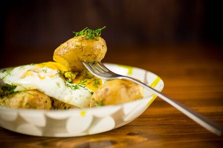 boiled early potatoes with fried egg and dill in a plateの写真素材