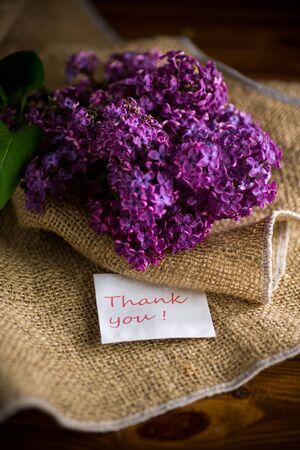 bouquet of beautiful spring purple lilac in burlap on a wooden tableの写真素材