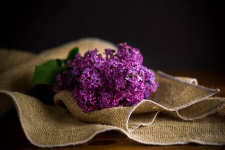 bouquet of beautiful spring purple lilac in burlap on a wooden tableの写真素材