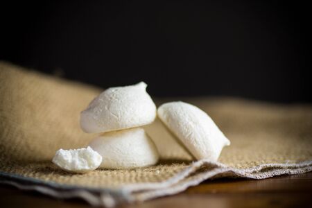 sweet tasty white meringues on a wooden table with a burlap tableclothの写真素材